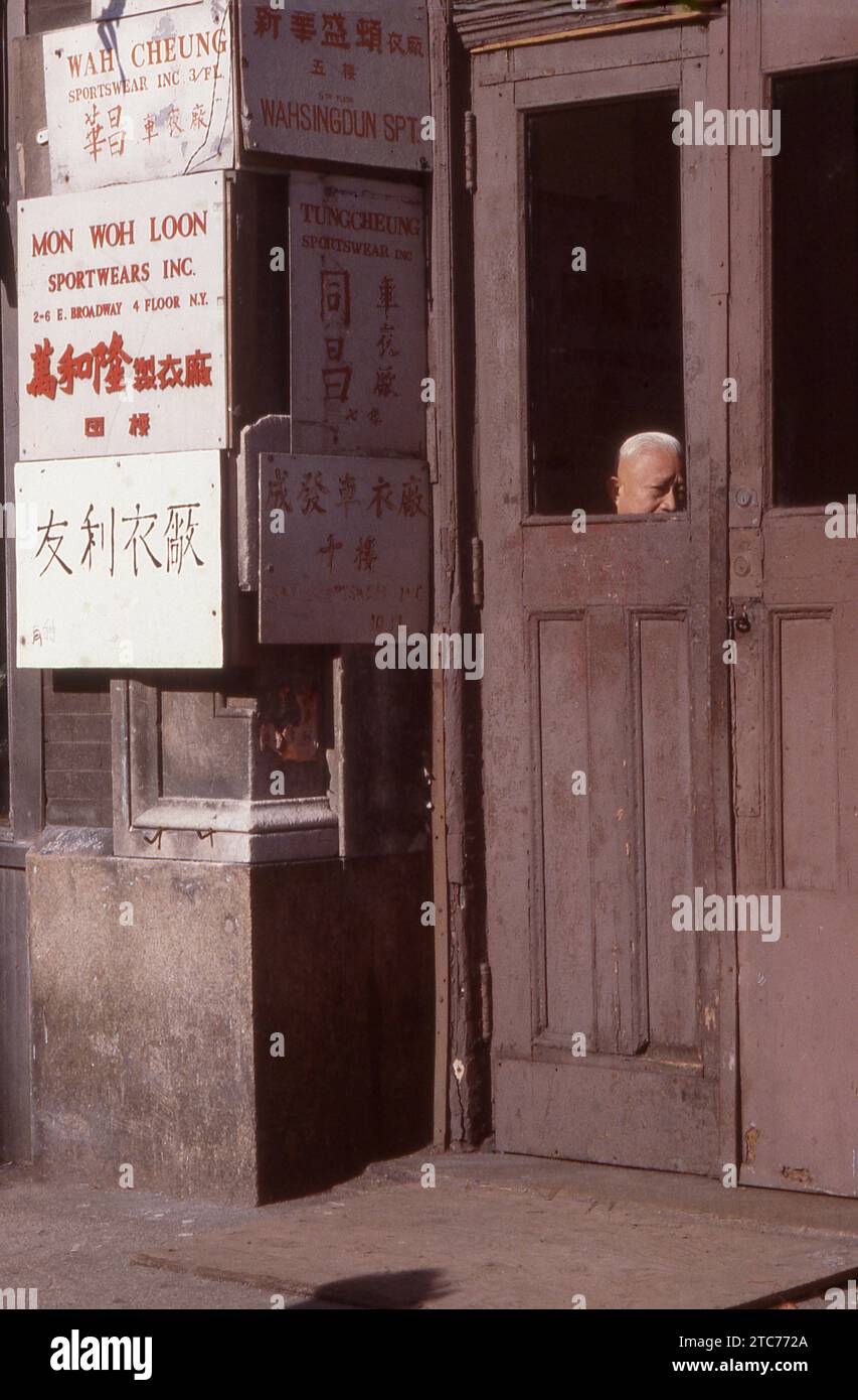 A winter 1979 street scene on East Broadway in Chinatown showing some business signs and an older Chinese man looking out of a window. Stock Photo