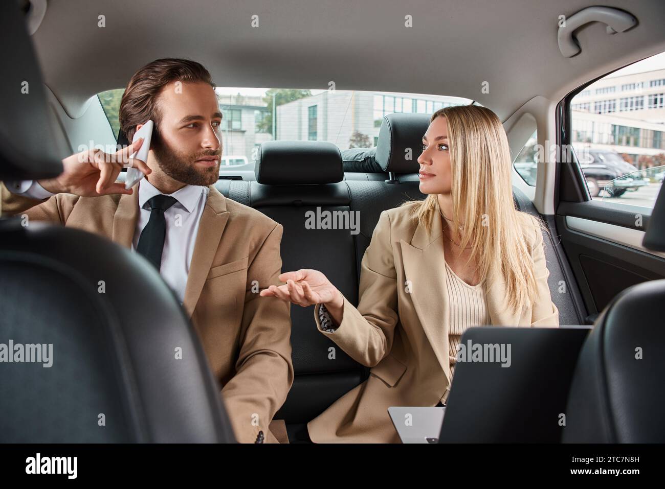 blonde businesswoman talking to handsome man in formal wear calling on smartphone in luxury car Stock Photo