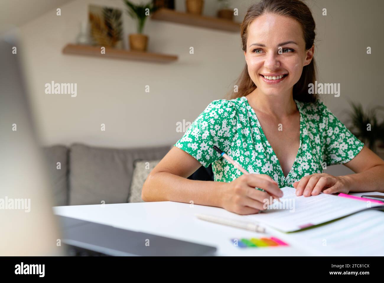 Adult student e-learning. Attractive brunette woman Smiling while Using Workbook at home desk. Educational Elegance. Stock Photo