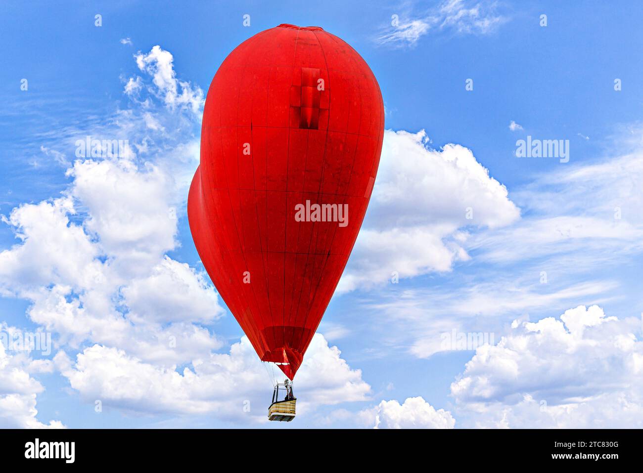 Red heart-shaped hot air balloon flying over a blue sky with white ...