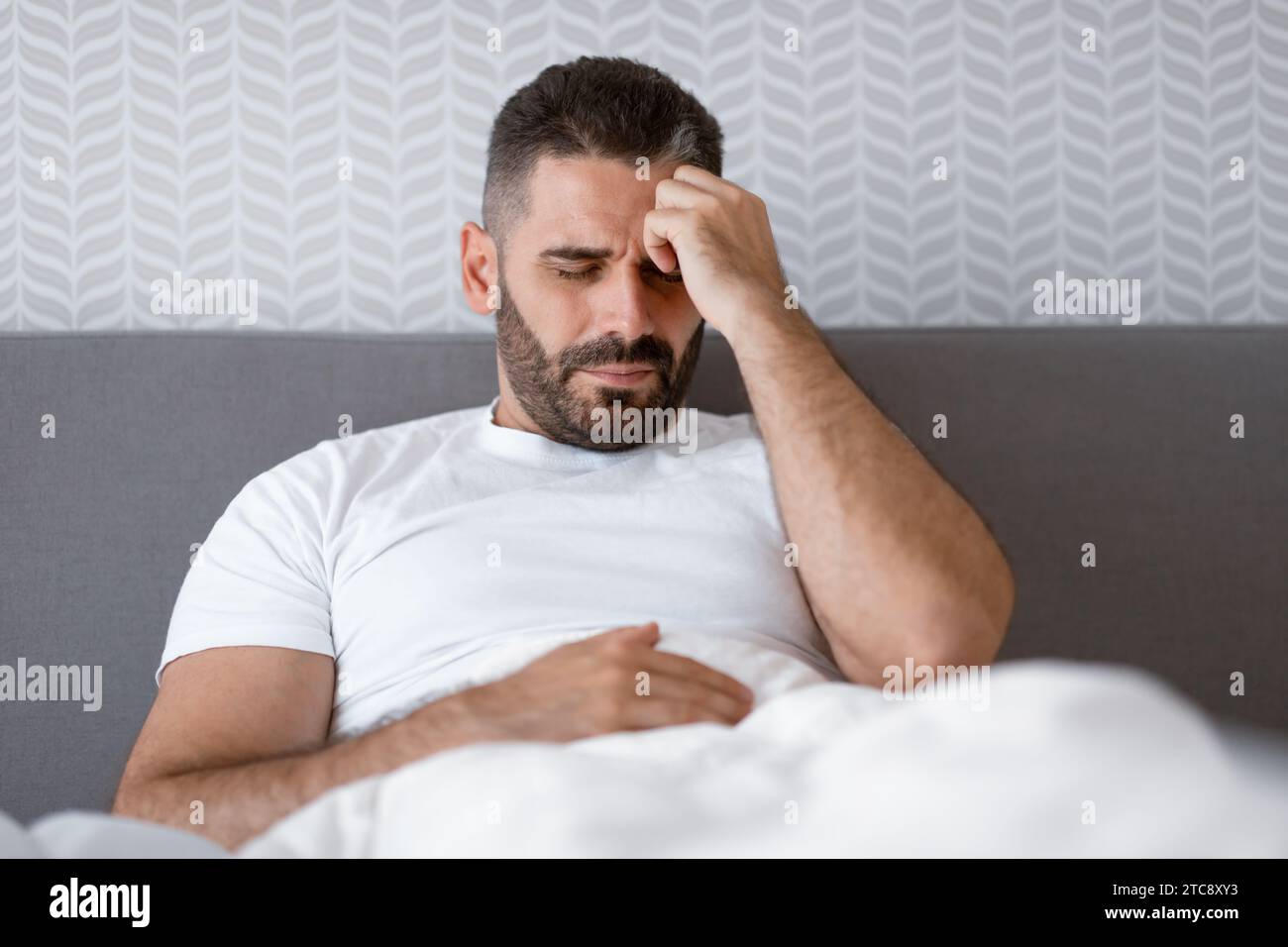 Unhappy man lying in bed touching head having migraine indoor Stock Photo