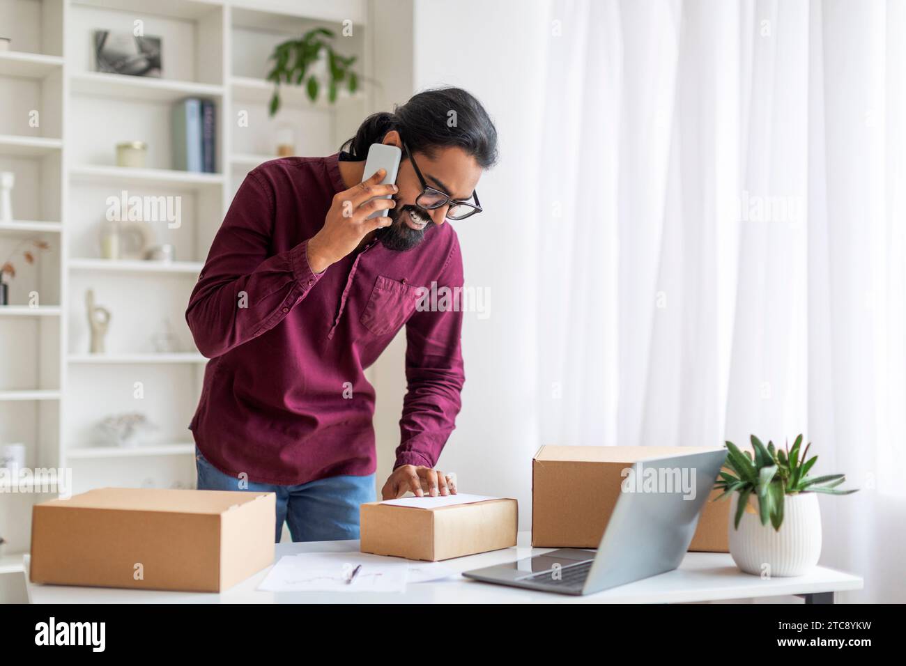 Indian Man Talking On Cellphone And Checking Packed Boxes With Orders Stock Photo