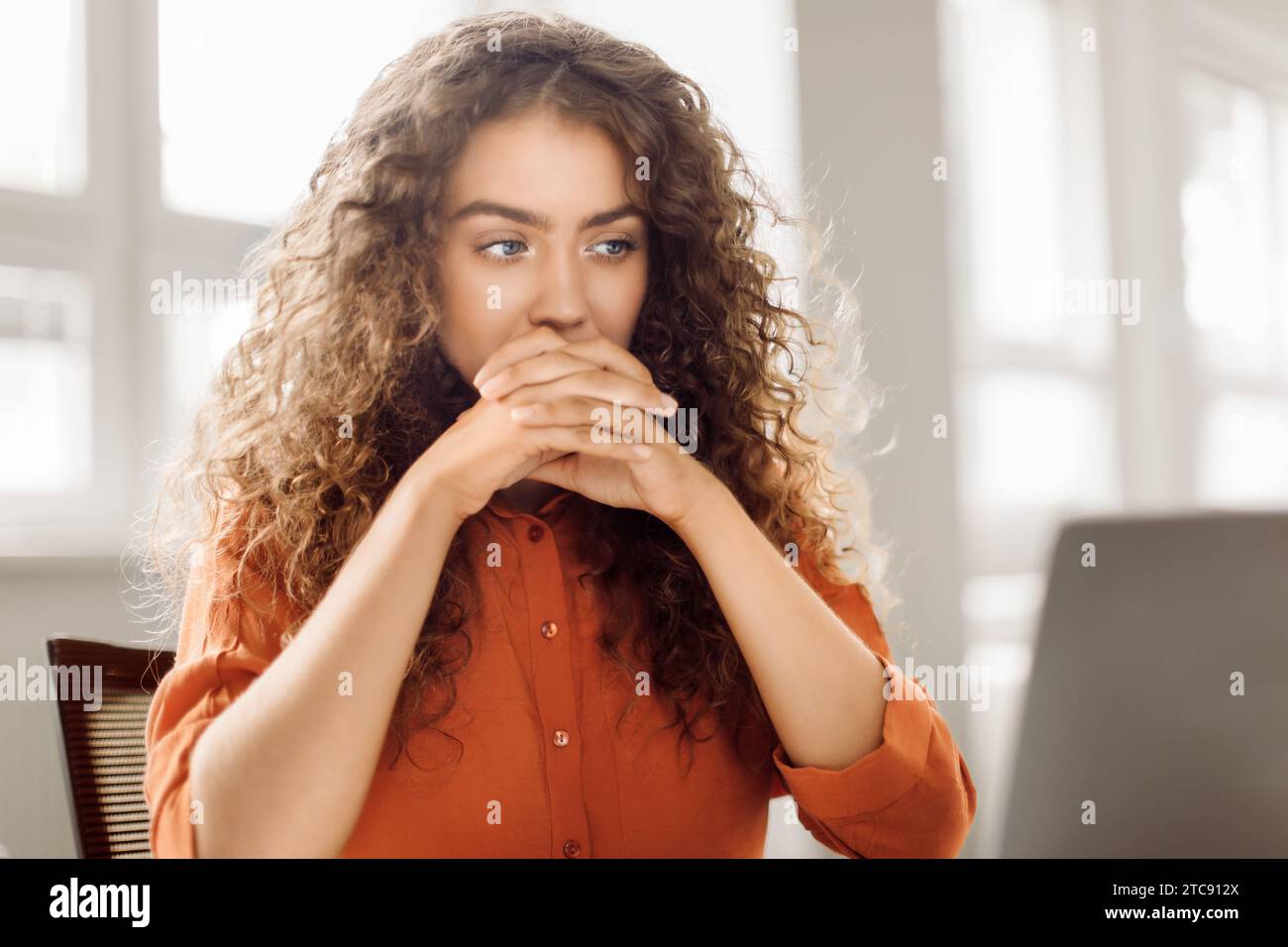 Curly-haired woman deep in thought at computer Stock Photo
