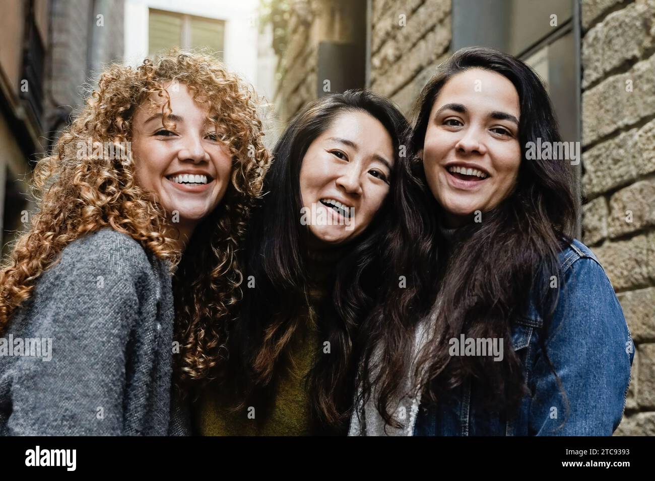 Three young women smiling at camera outdoors in city. Multiracial ...
