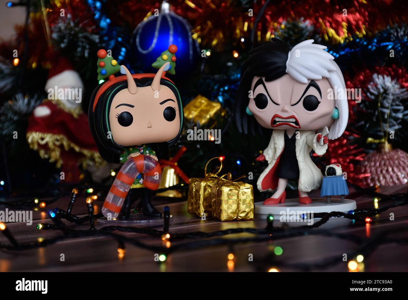 Funko Pop action figures of Mantis from Guardians of the Galaxy and Disney villain Cruella de Vil. Christmas tree, gift boxes, colorful lights. Stock Photo