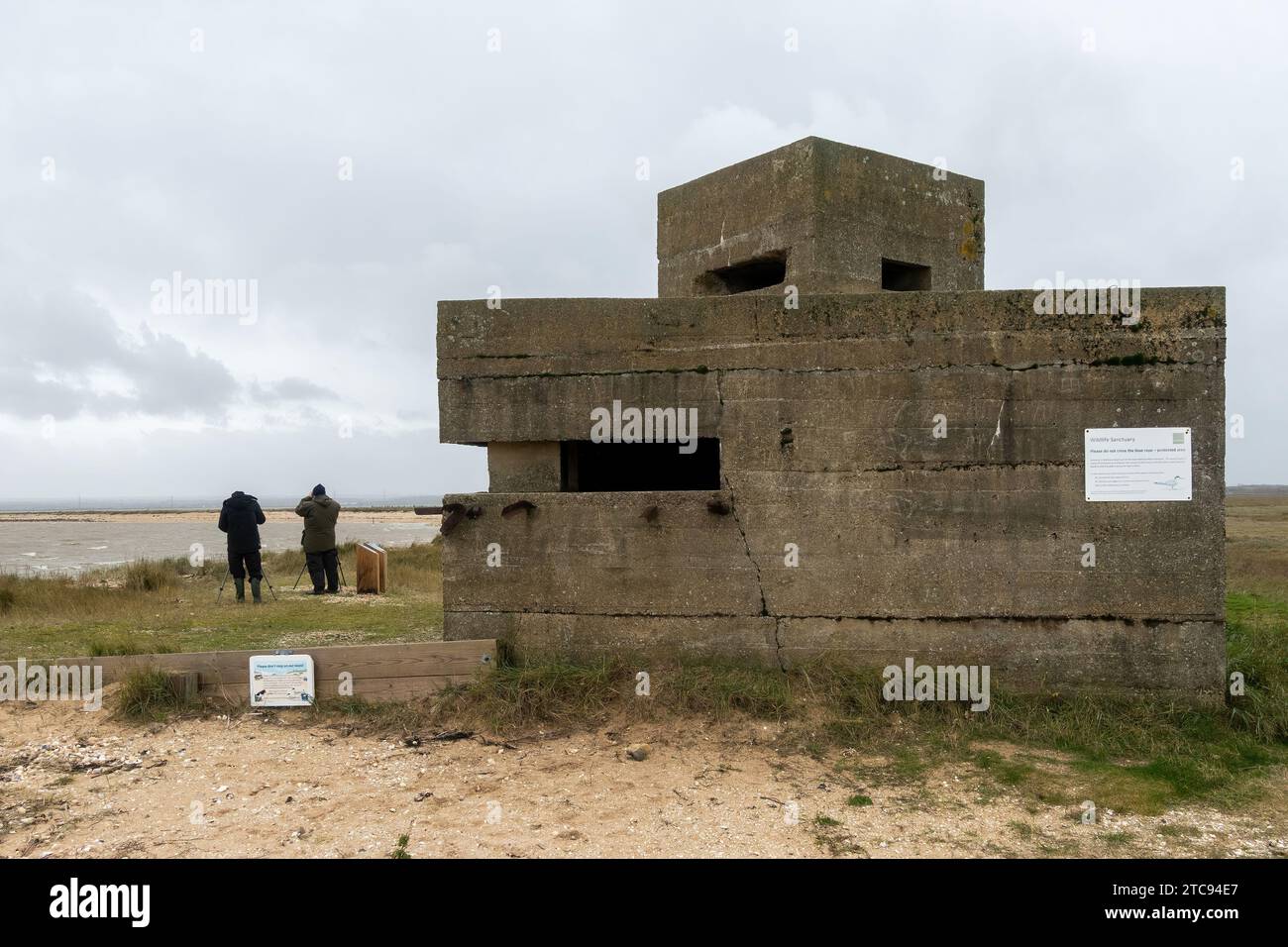Two birdwatchers next to the old bunker at Swale National Nature Reserve, a coastal wildlife site on the Isle of Sheppey, Kent, England, UK Stock Photo