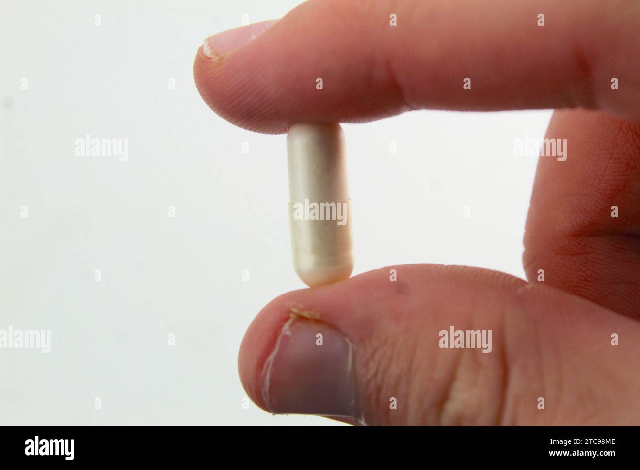 A close up photo of a person holding a white pill between their two fingers. Stock Photo
