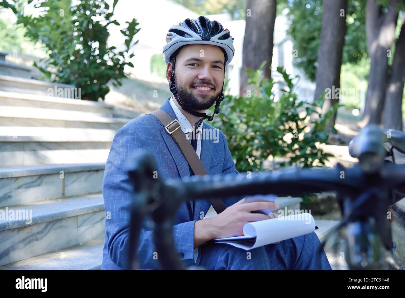 Young businessman in helmet sitting on stairs and analyzes business report. Business and working concept. Close up Stock Photo