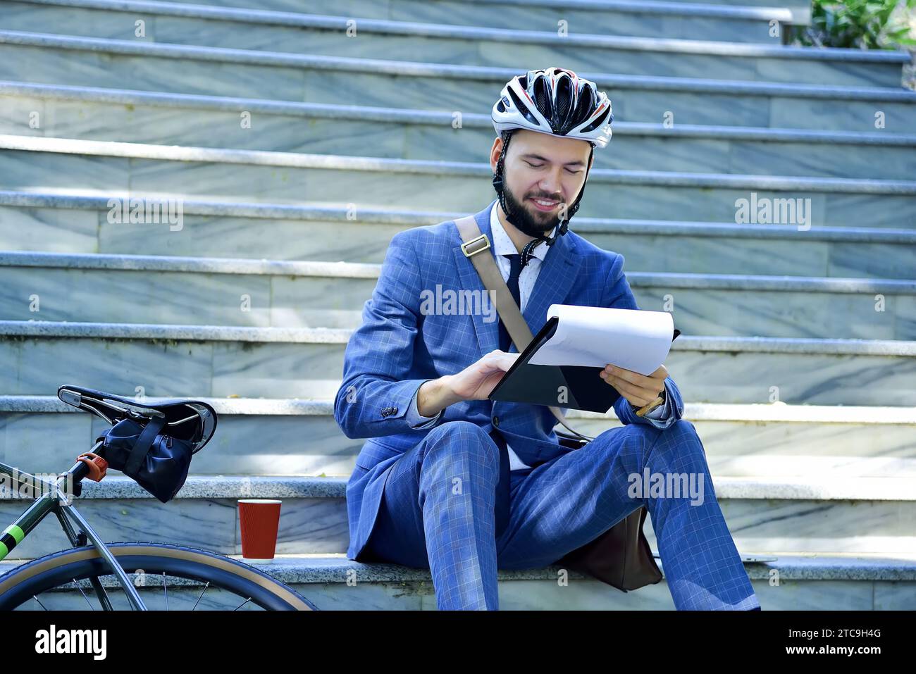 Businessman in helmet sitting on stairs and analyzes report. Business and working concept Stock Photo