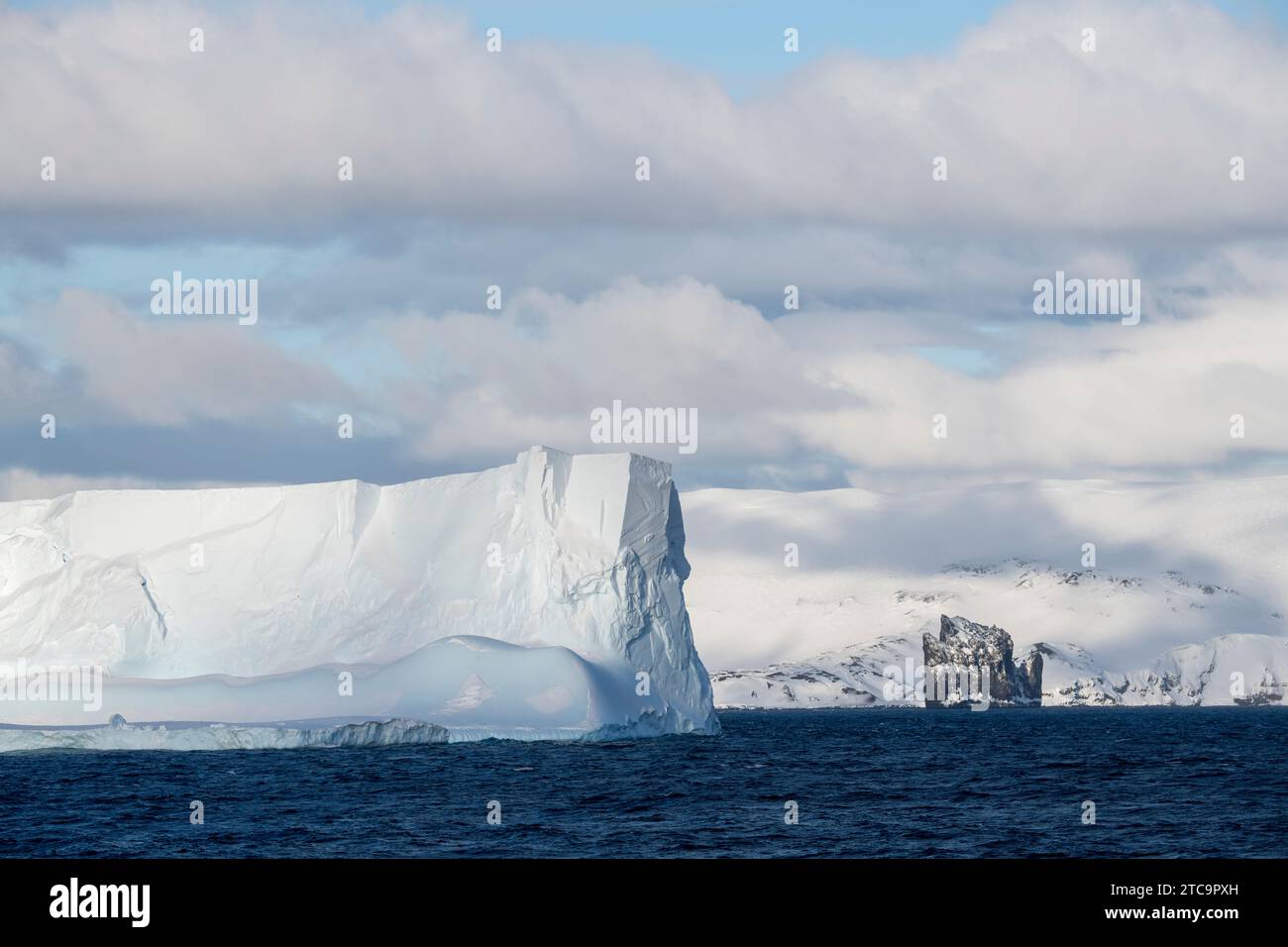 Antarcica, South Shetland Islands, Bransfield Strait. Large iceberg and New Rock with coastal view of Deception Island in the distance. Stock Photo