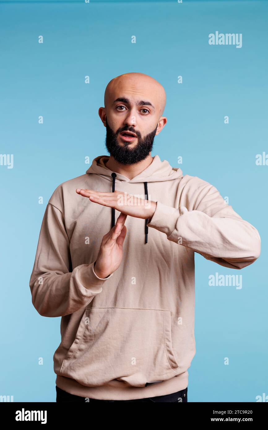 Young arab man taking break while showing time out gesture portrait. Person in casual hoodie clothes stopping communication with interruption signal and looking at camera Stock Photo