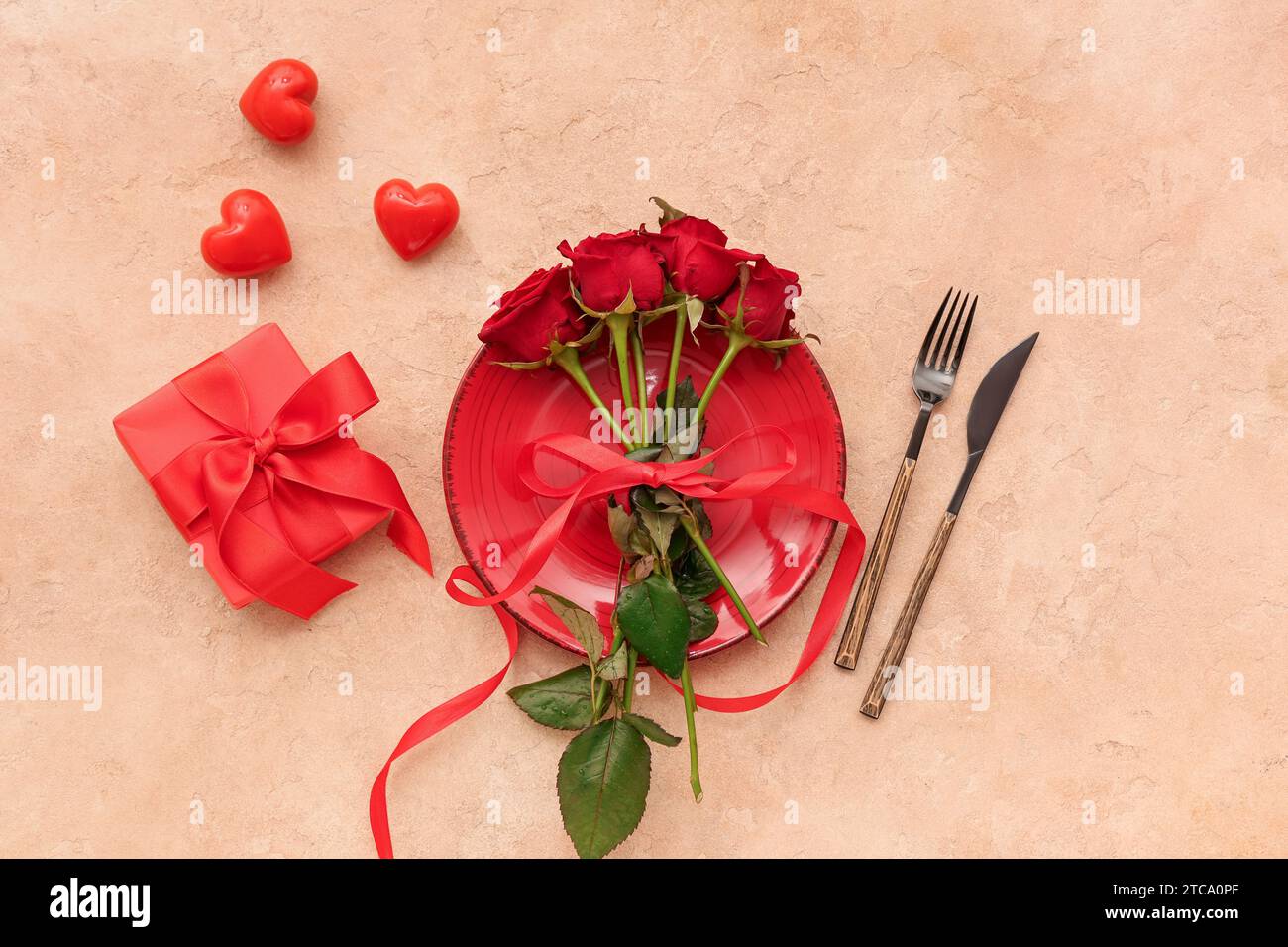 Beautiful table setting with red roses, gift box and hearts on beige ...