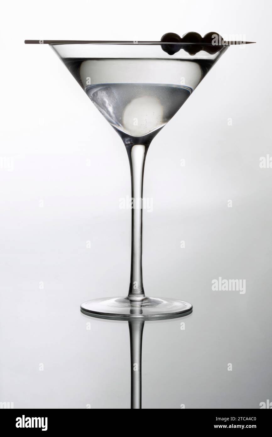 Martini mixed drink with olive garnish on a light grey background with