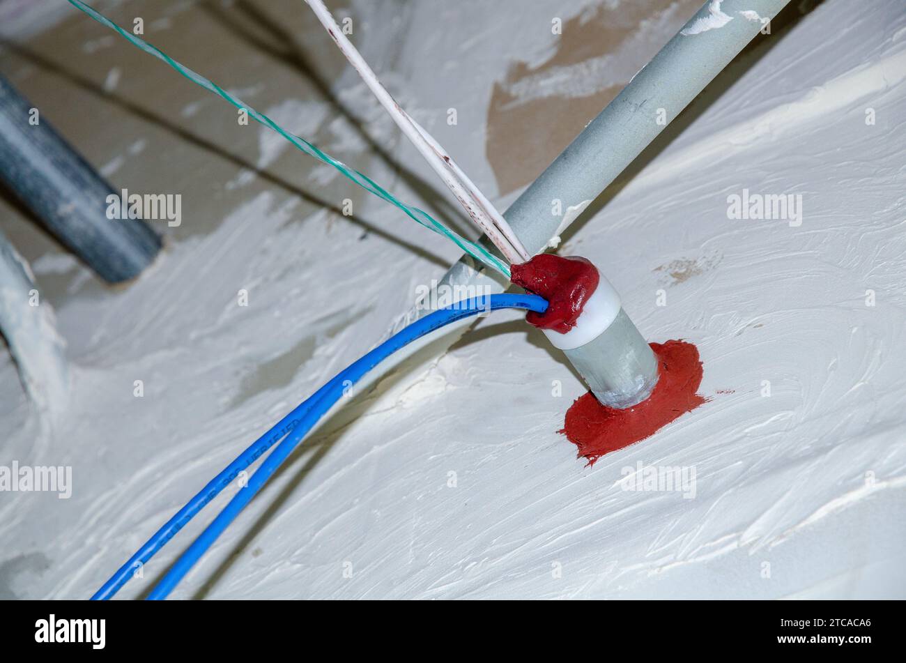 Red firestop sealant on firerated wall next to electrical conduit Stock