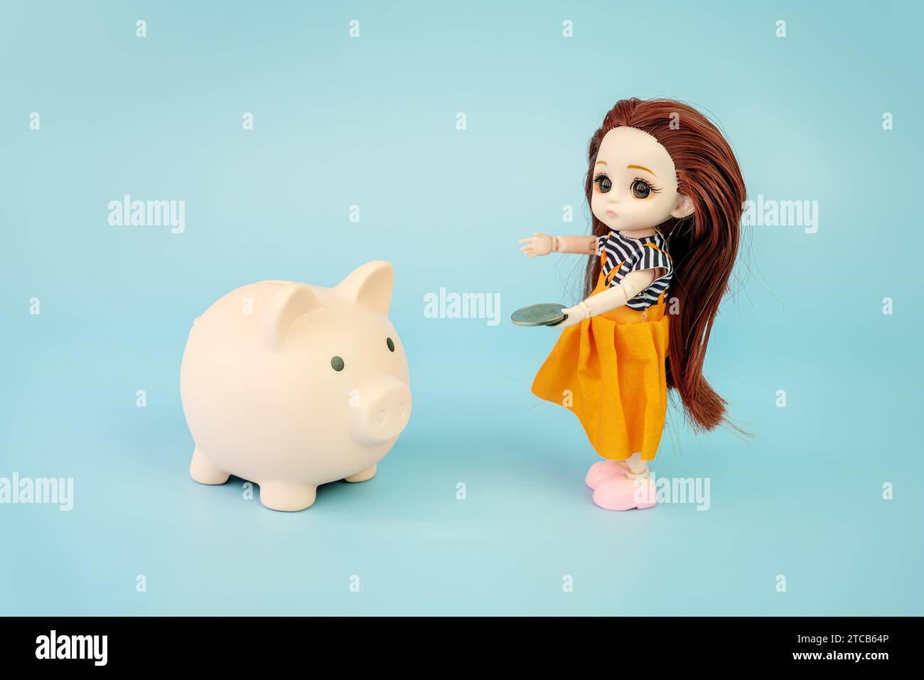 pink piggy bank and doll on a blue background. Concept of increasing income from bank accounts, savings. A small child doll with a coin in her hands o Stock Photo