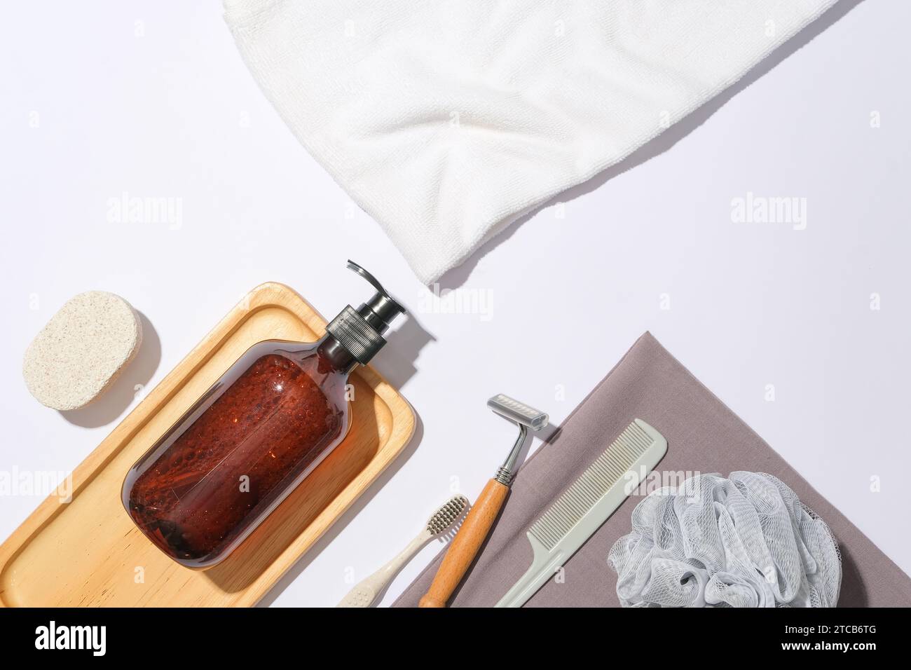 A bottle of shampoo is placed on a wooden tray and toiletries are displayed on a delicate white background. Advertising with space inside the bathroom Stock Photo