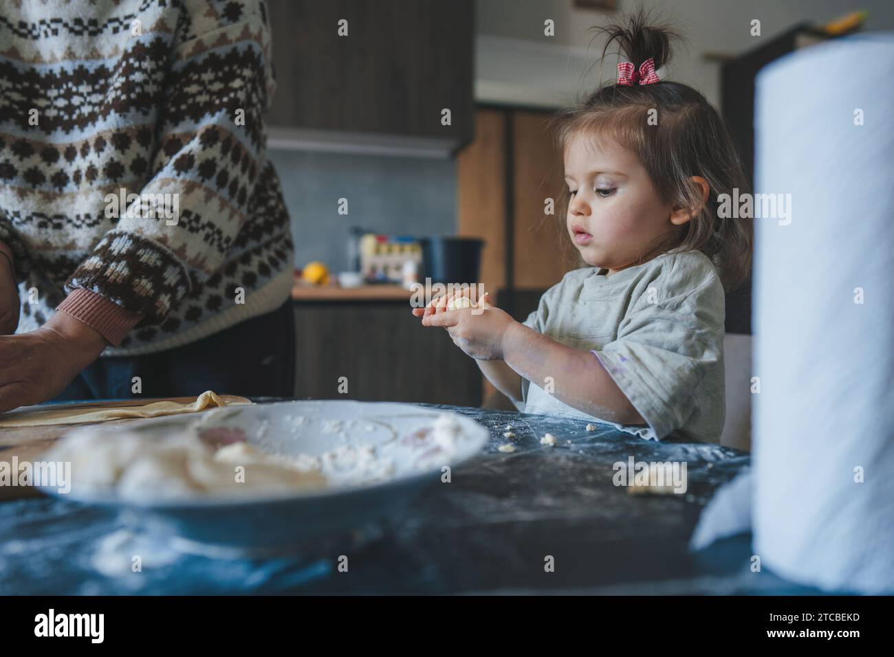 Child Helping In Kitchen Cute little girl sitting in the kitchen near her grandmother sculpting ...