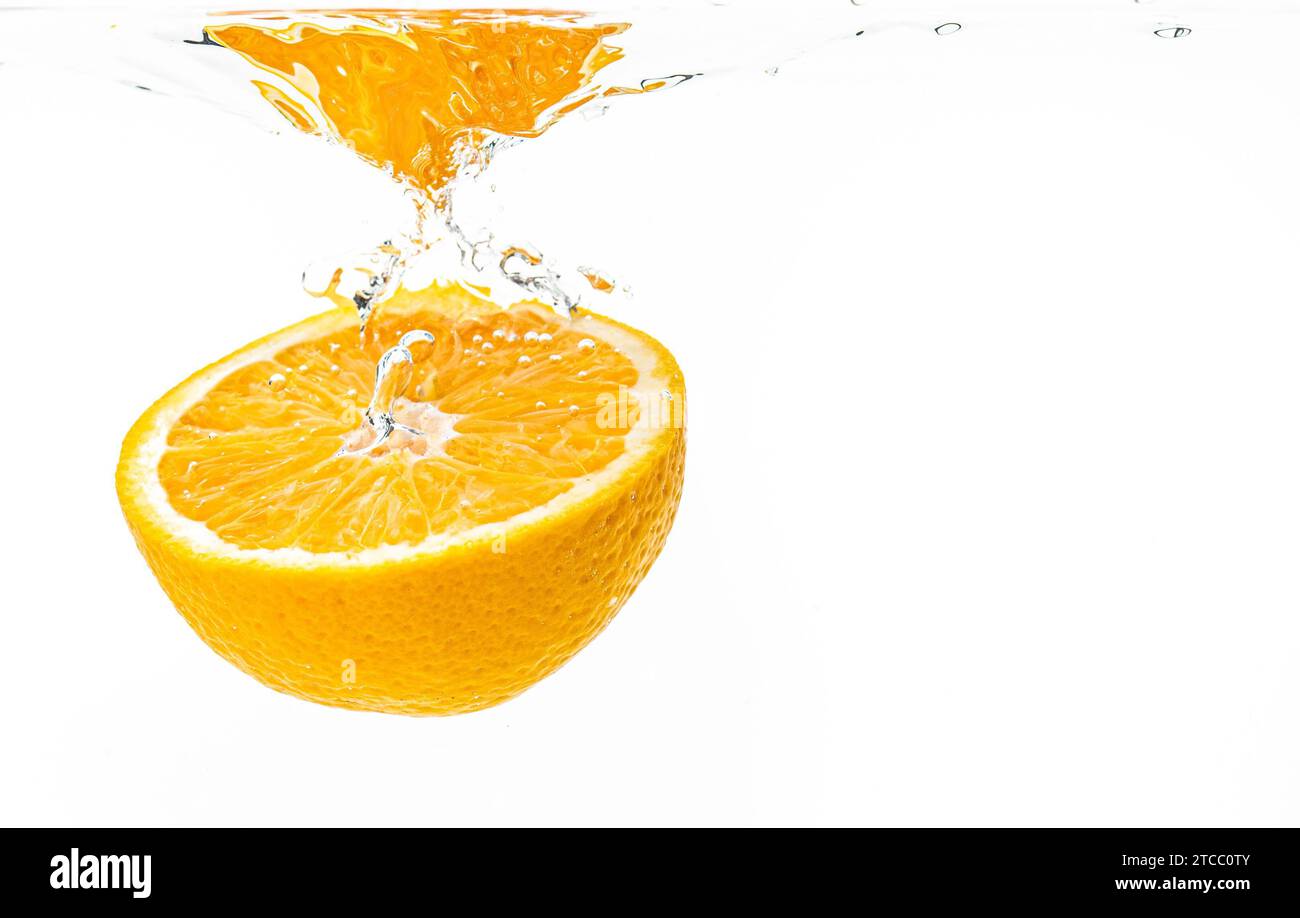 Fresh ripe half of orange fruit sinking in the clear water, isolated on white background. Health food concept Stock Photo