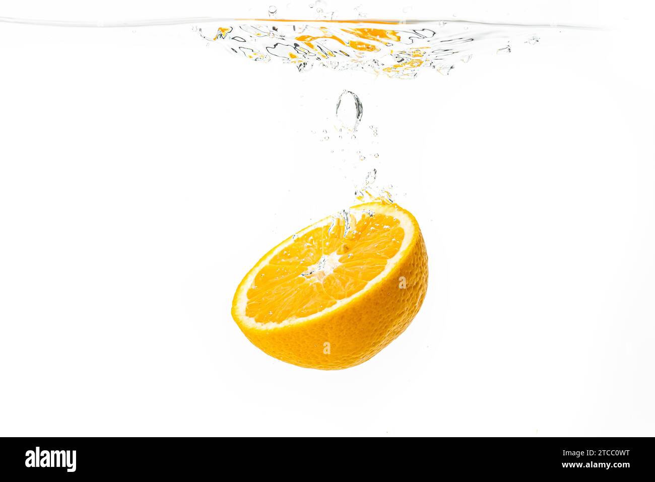 Fresh ripe half of orange fruit sinking in the clear water, isolated on white background. Health food concept Stock Photo