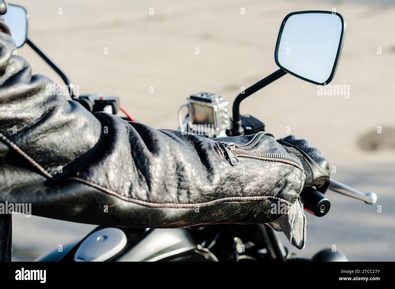 Hands of a motorcyclist in a black leather jacket and gloves on the handlebars of a motorcycle Stock Photo