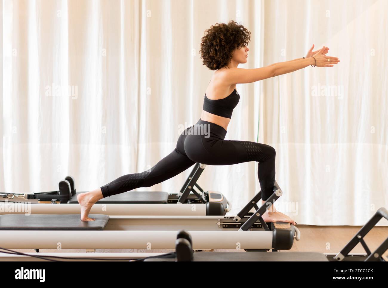 Concentrated fit female stretching legs and doing lunge exercises on pilates  reformer during training in gym stock photo