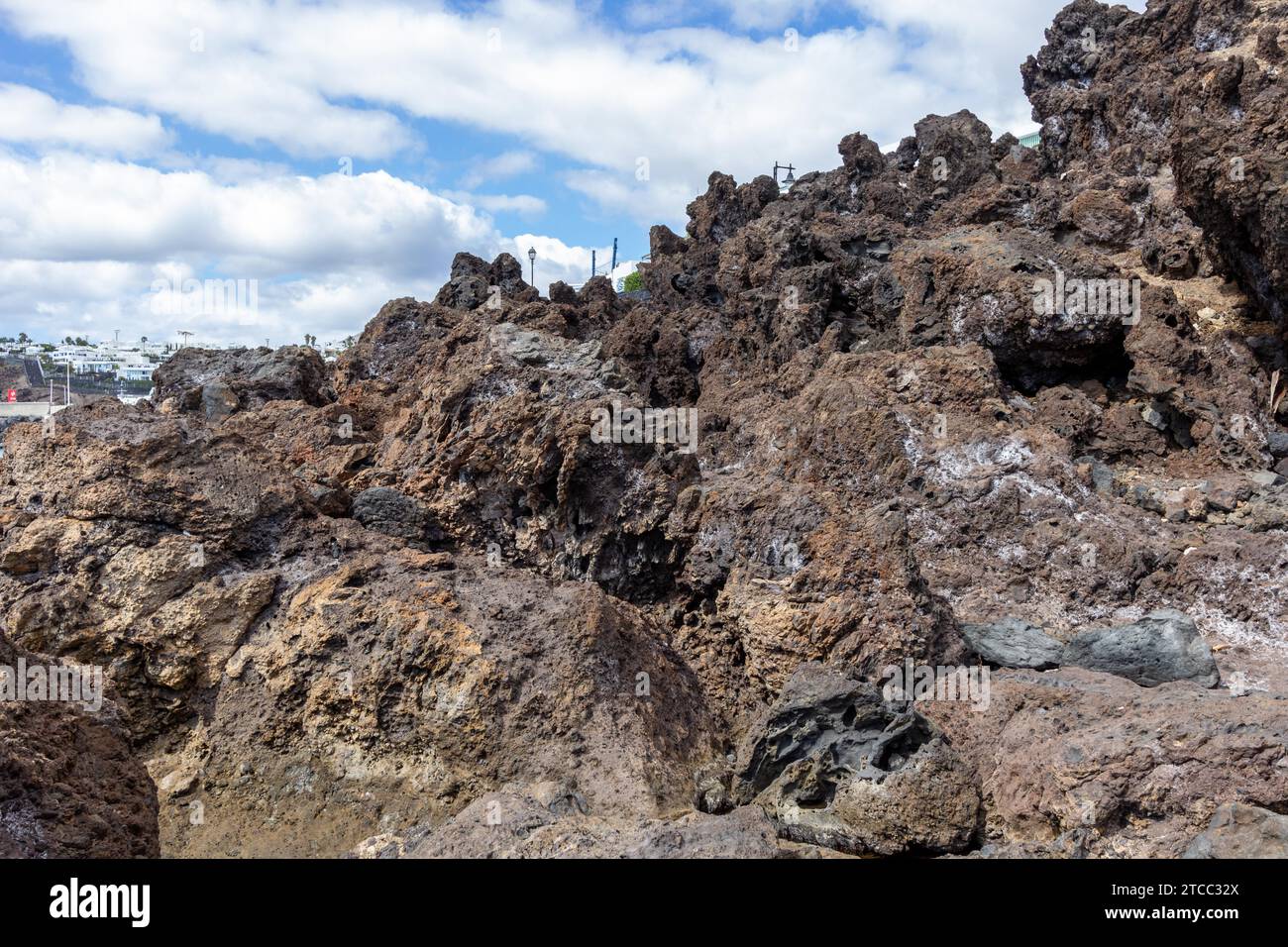 Big lava rocks on the coastline of Puerto del Carmen at Canary island Lanzarote, Spain. The sky is blue with white clouds Stock Photo