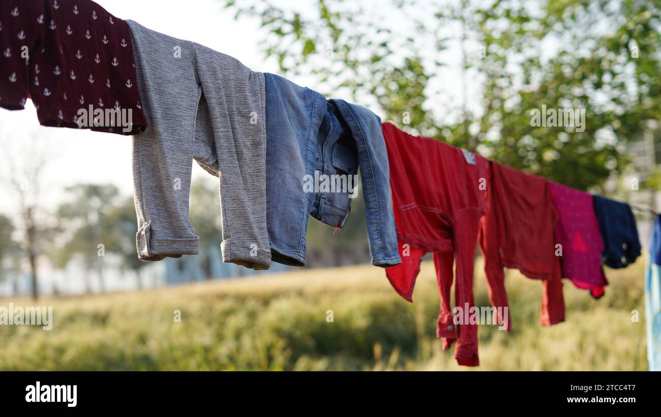 After being washed, Colorful clothing dries on a clothesline in the yard outside in the sunlight. Clothesline with freshly washed clothes outdoors in Stock Photo