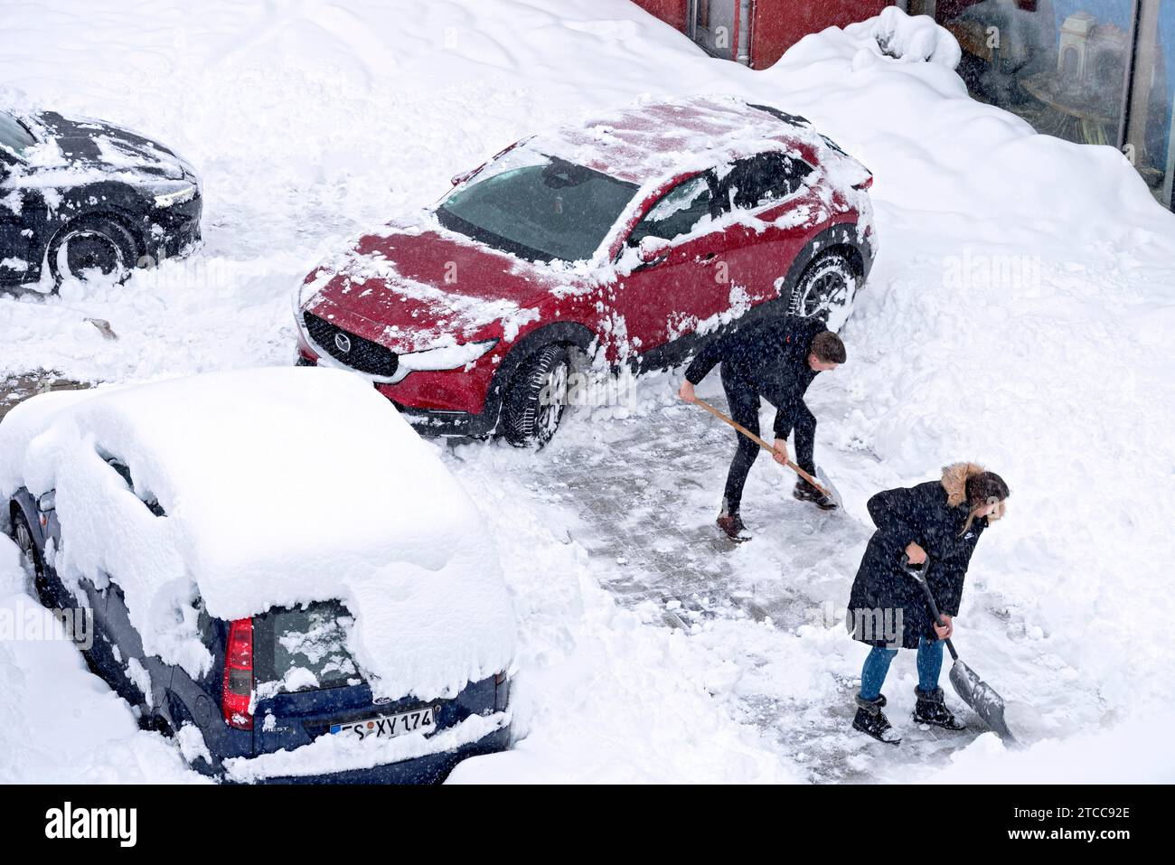 Man and woman shovelling snow on car park, car, car, snowed in, fresh snow, heavy snowfall, snow masses, snow chaos, snow shovel, onset of winter Stock Photo