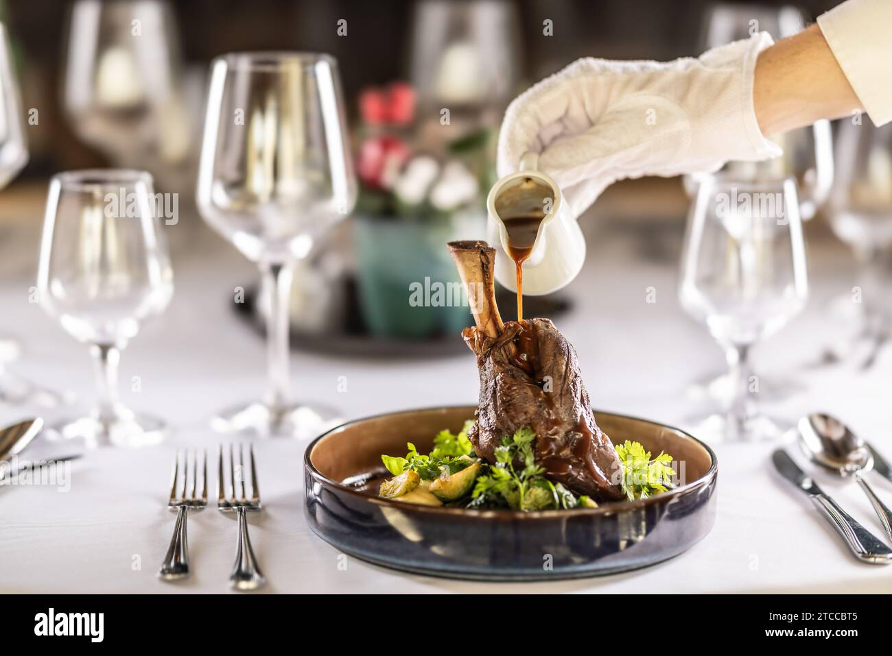 The chef or waiter finishes the meal right on the restaurant table, pouring the sauce over the leg of lamb confit. Stock Photo