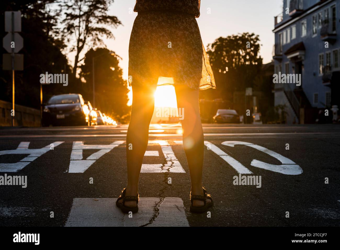 The sun shines brightly through a woman's legs as she watches it set from a hill in San Francisco USA Stock Photo