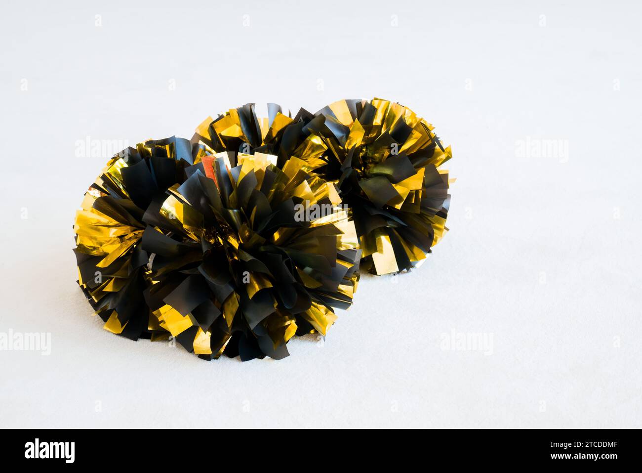 Gold and black cheerleading pom-poms on white practice mat. Background Stock Photo