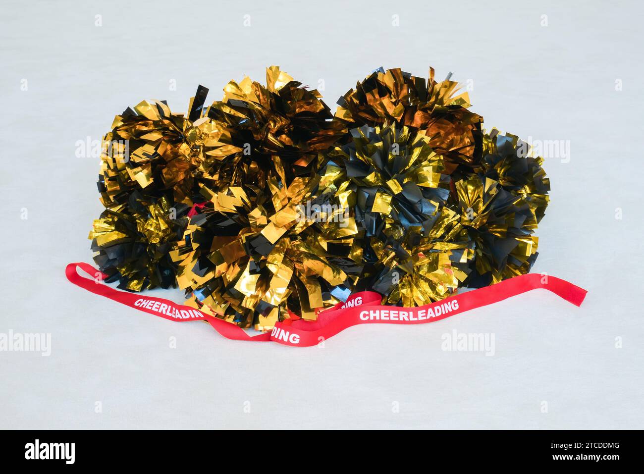 Gold and black pompoms with a red cheerleading ribbon on a white practice mat Stock Photo