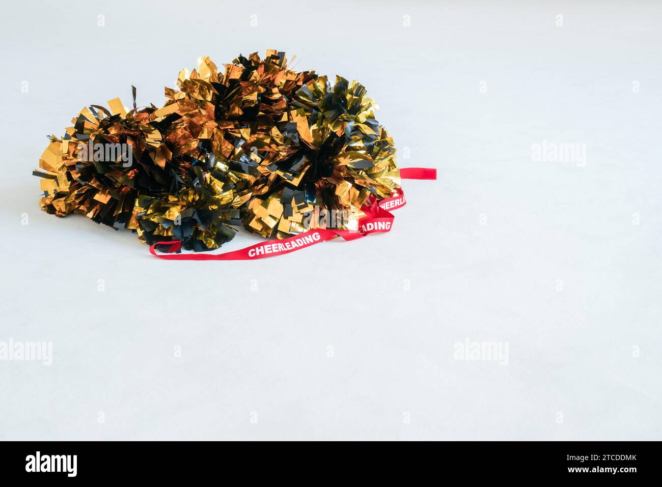 Gold and black pompoms with a red cheerleading ribbon on a white practice mat. Background Stock Photo