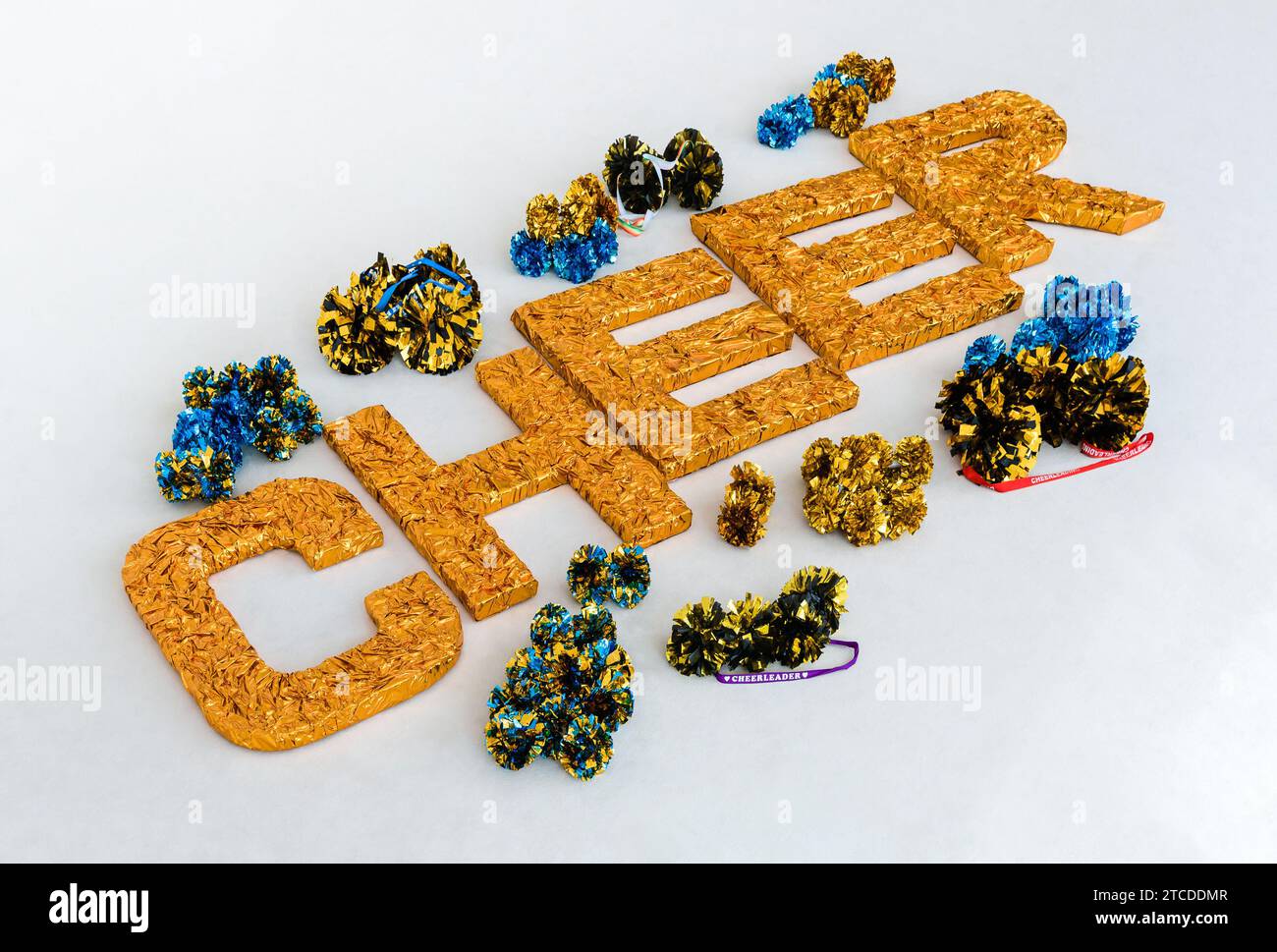 Large gold letters 'CHEER' on a white training mat surrounded by cheerleading pom-poms in different colors Stock Photo