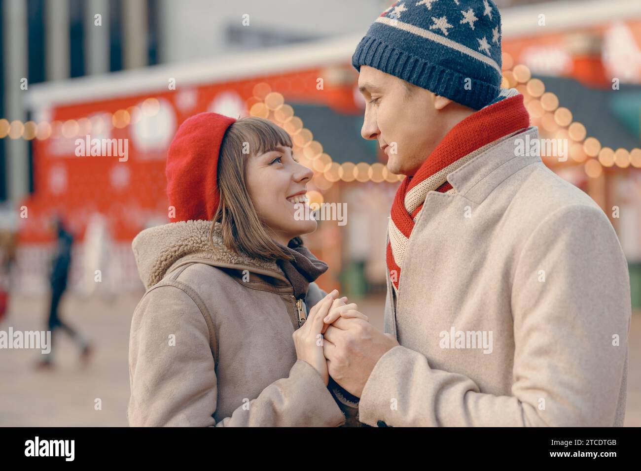 Smiling couple holding hands with a picturesque Christmas market behind them Stock Photo