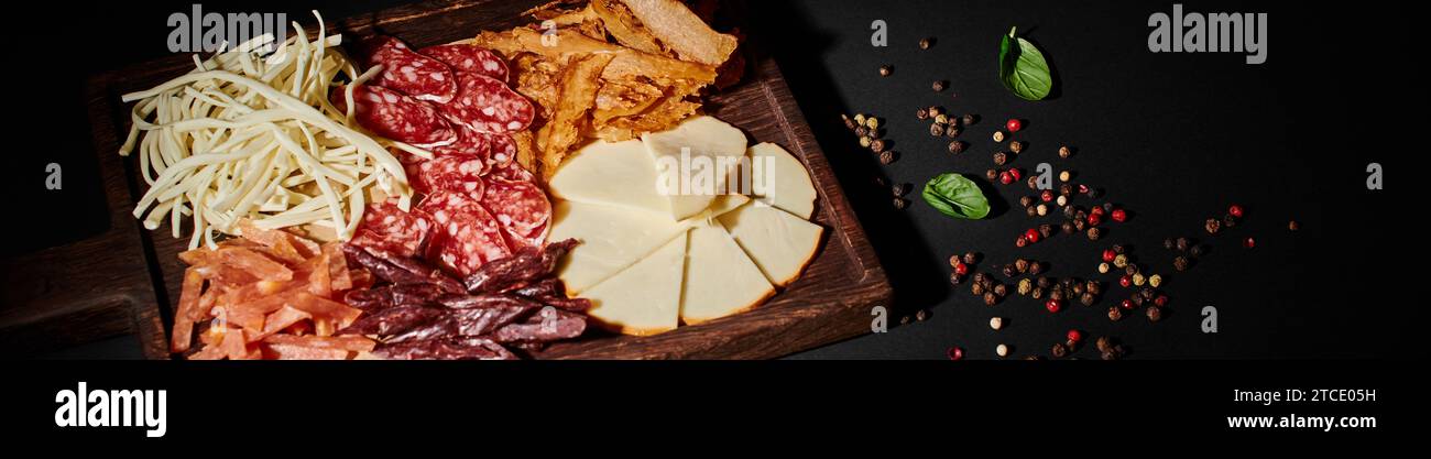 banner of charcuterie board with gourmet cheese selection, dried beef and salami slices on black Stock Photo