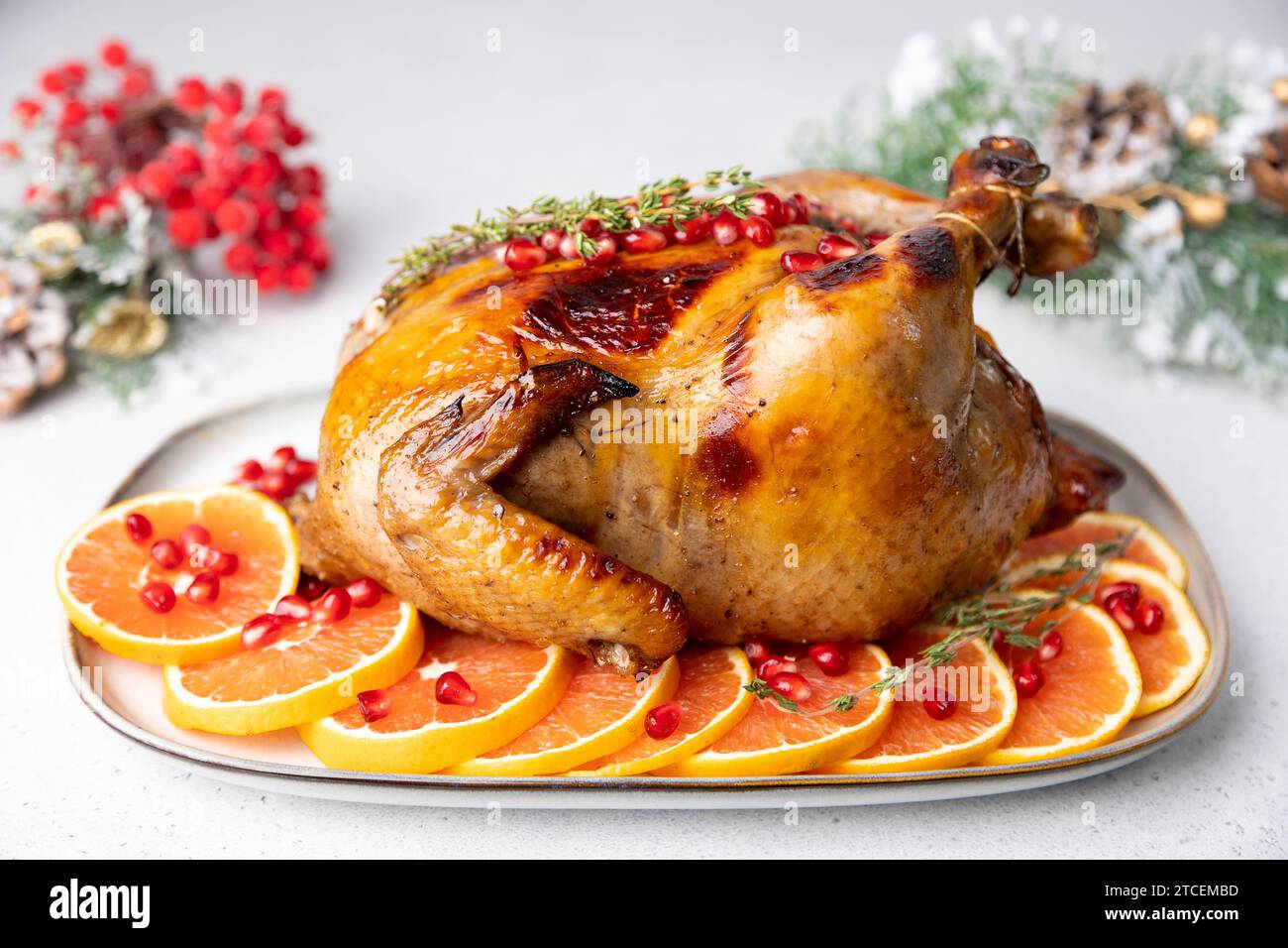 Chicken baked whole to appetizing crispy crust with pomegranate and red orange. Traditional New Year and Christmas dish. In the background are Christm Stock Photo