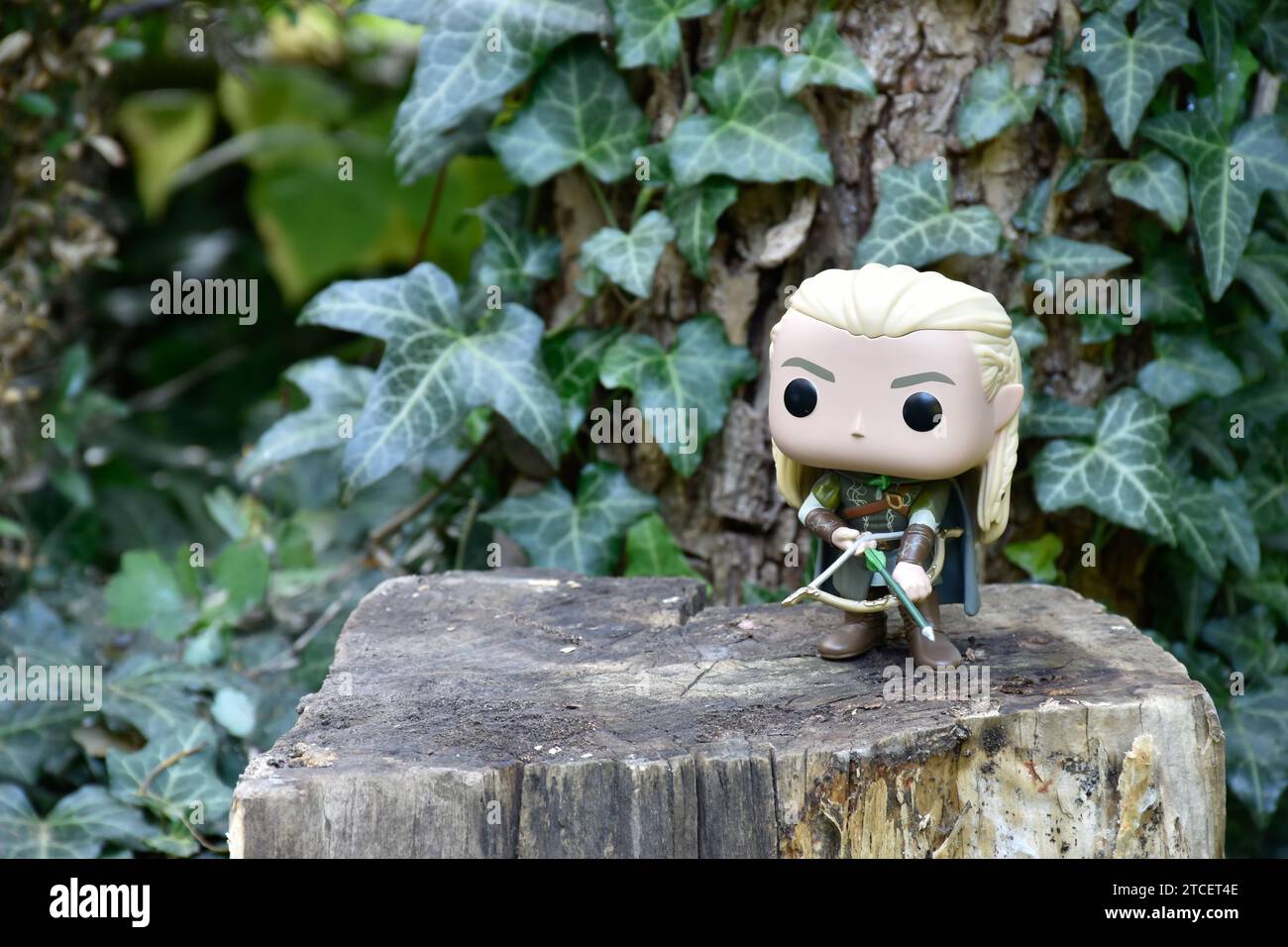 Funko Pop action figure of elf Legolas from fantasy movie The Lord of the Rings. Warrior holding bow and arrow. Forest tree, green ivy leaves. Stock Photo