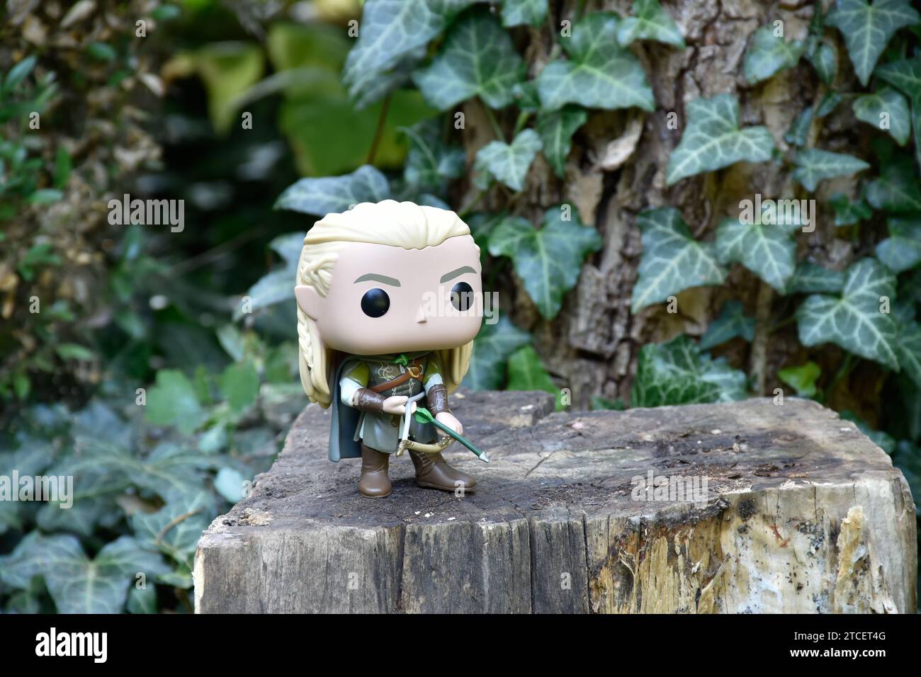 Funko Pop action figure of elf Legolas from fantasy movie The Lord of the Rings. Warrior holding bow and arrow. Forest tree, green ivy leaves. Stock Photo