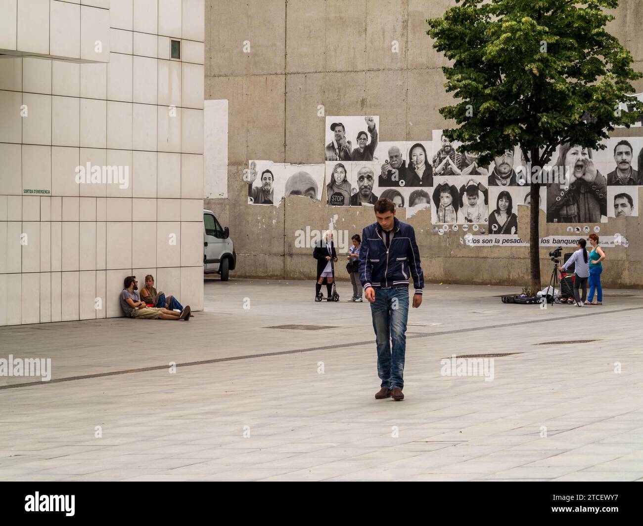 A head-down passerby and a film crew outside the Museum of Contemporary Art in Barcelona, Spain. Stock Photo
