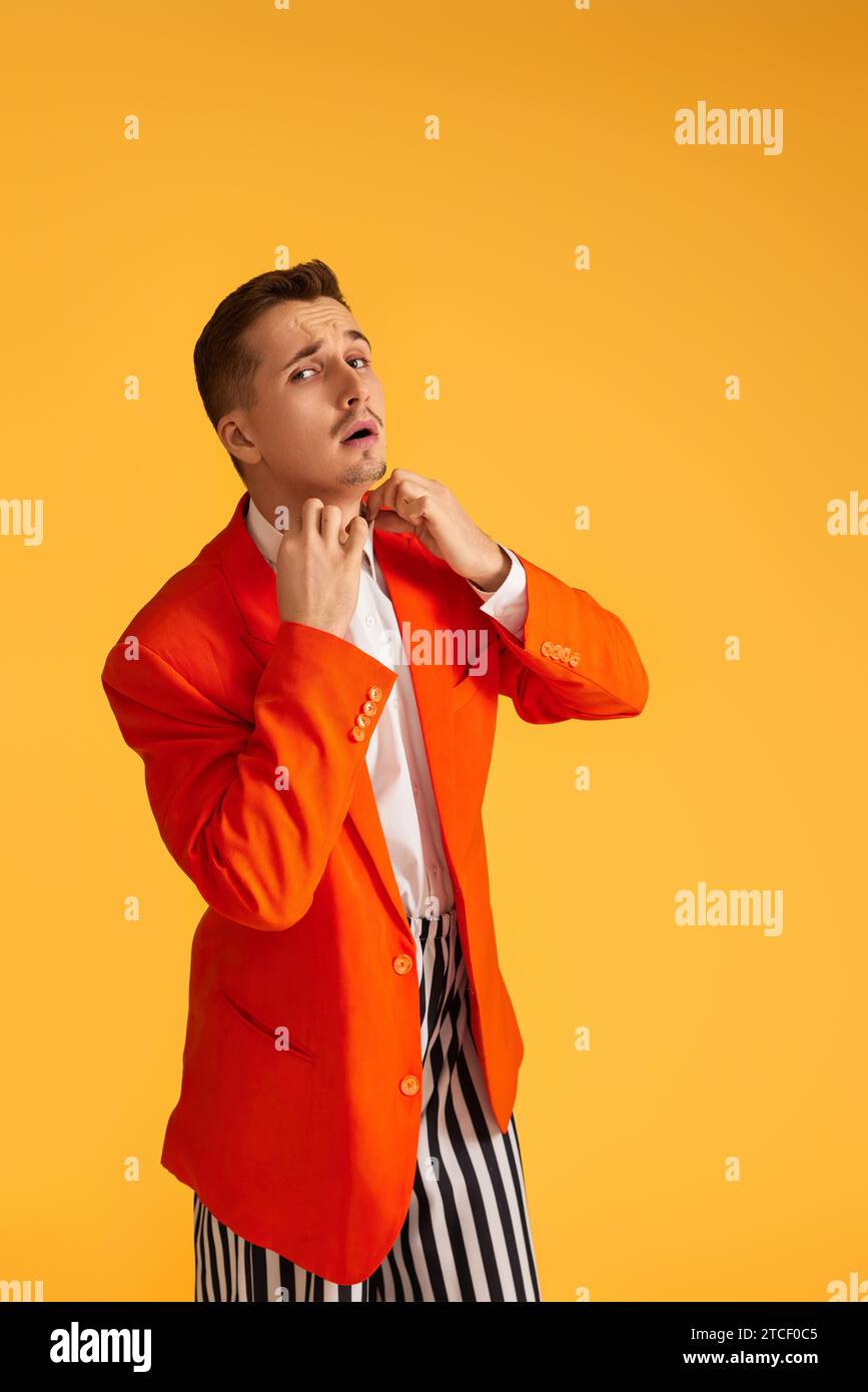 Cheerful funny young man in orange jacket and striped pants on yellow ...