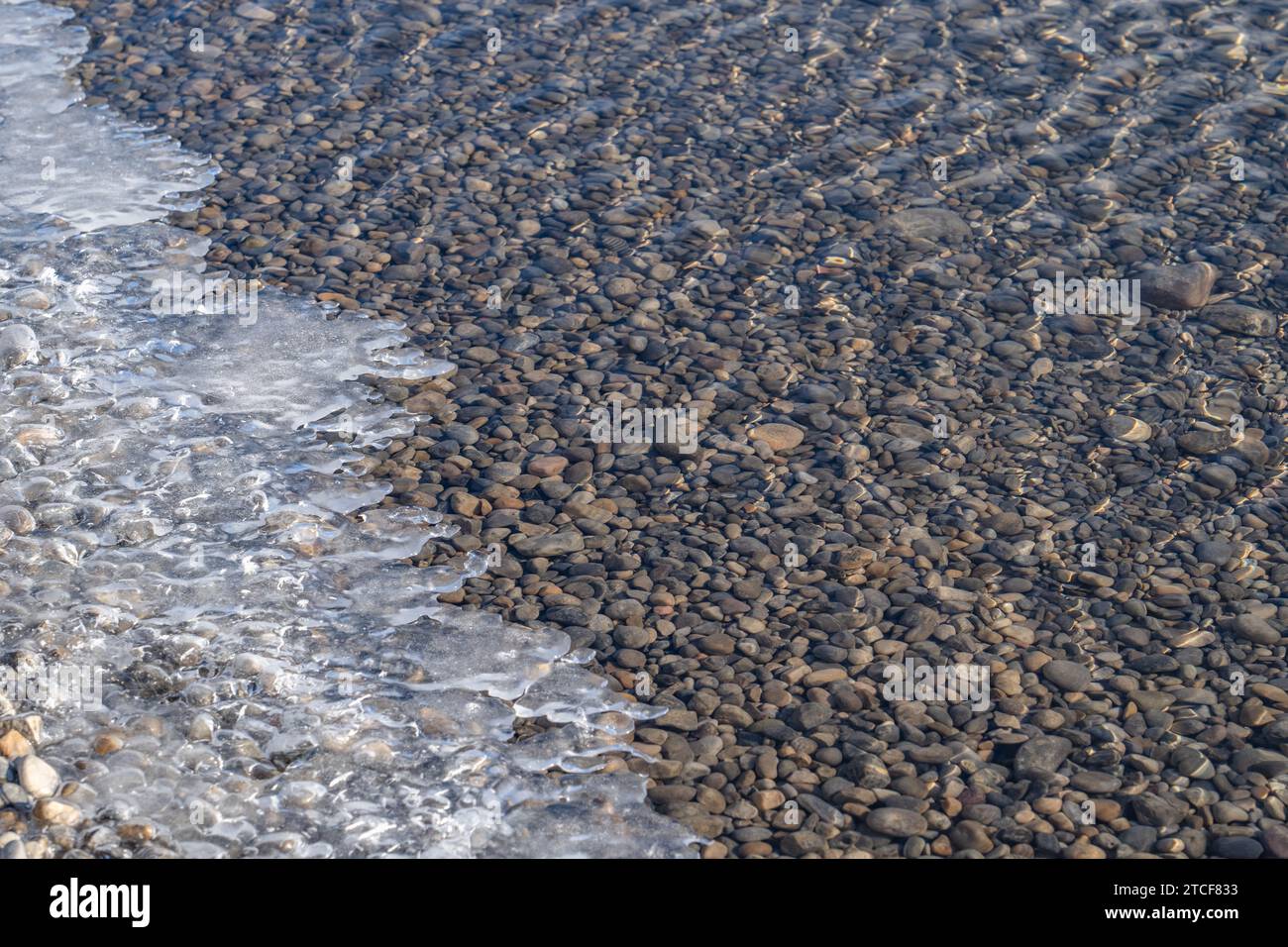 Ice forming at lake's edge, with clear water and stones Stock Photo