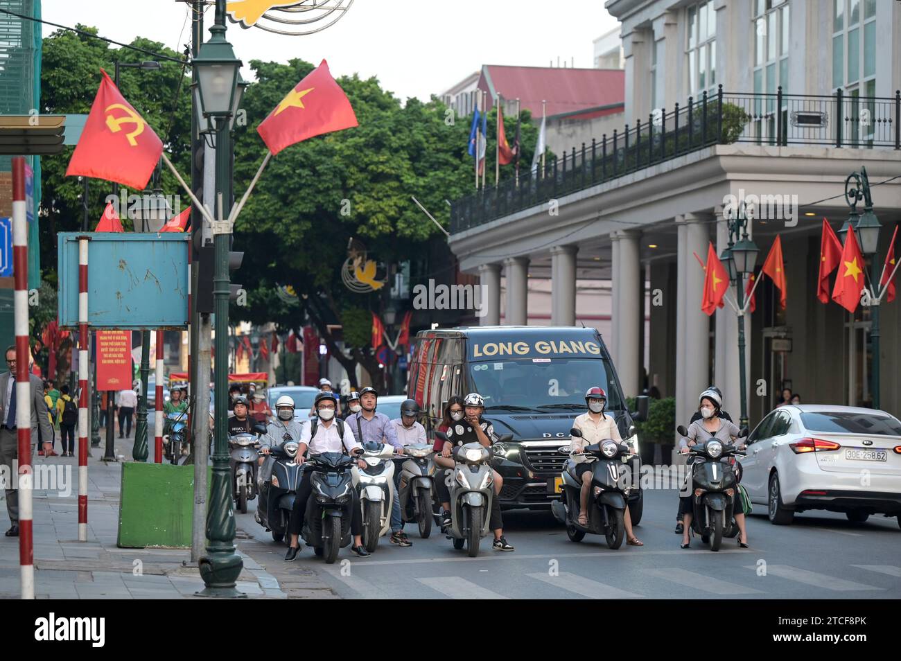 VIETNAM, Hanoi, french quarter, main street with red flag of communist party and Vietnam national flag with yellow star, traffic during rush hour, two-wheeler at crossing Stock Photo