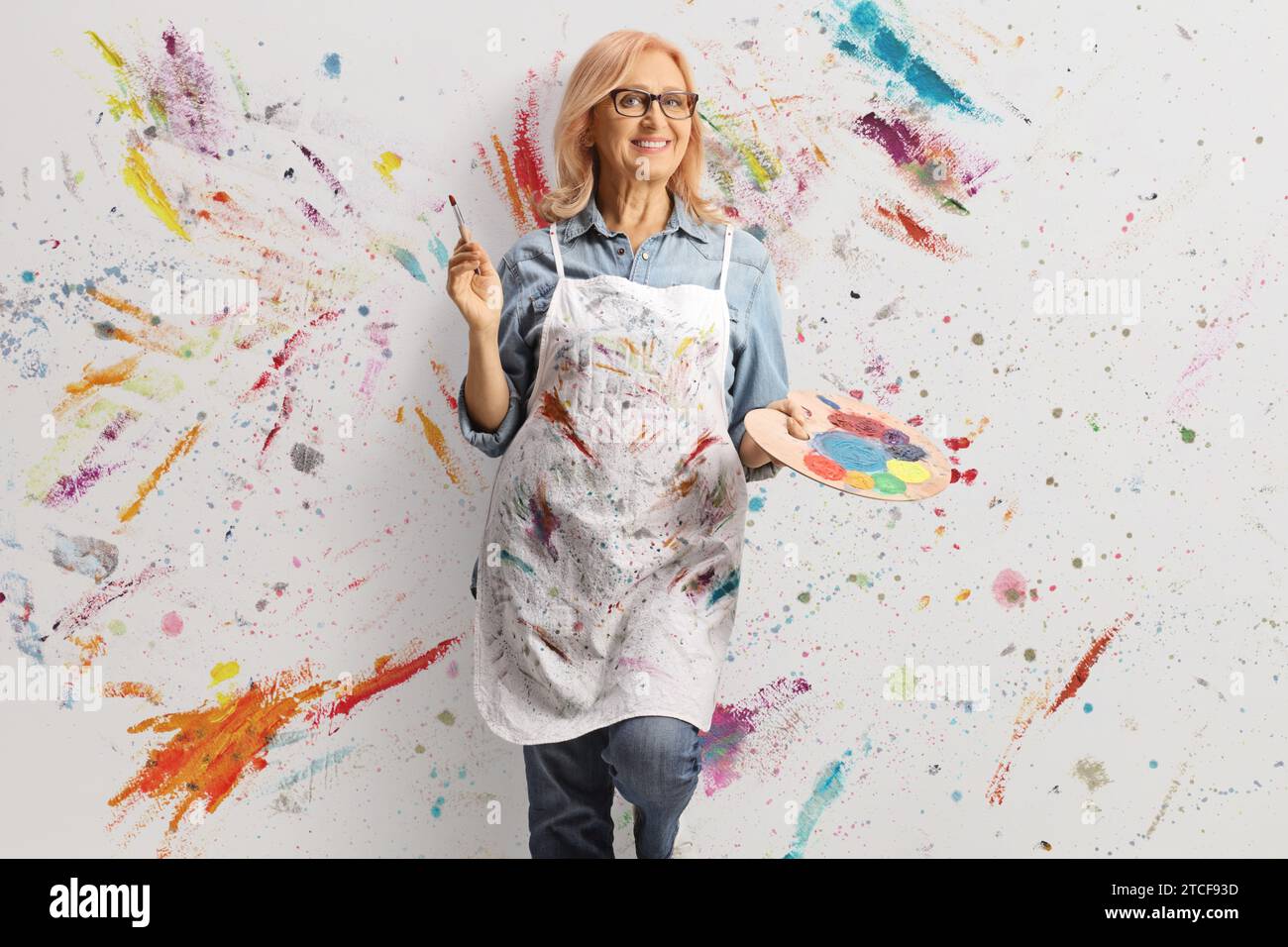 Happy middle aged woman leaning on wall with paint and holding a brush and palette Stock Photo