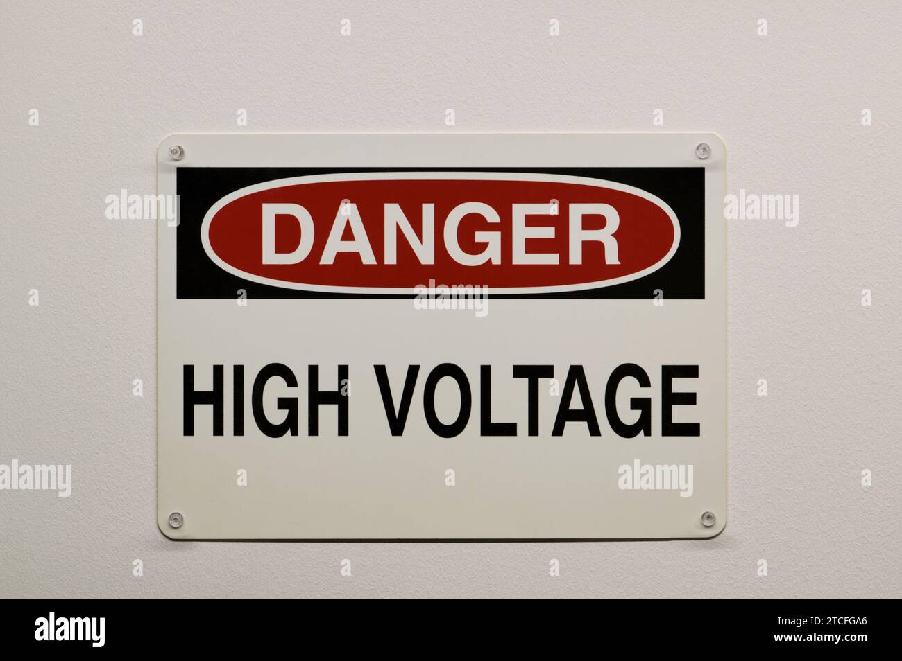 Danger High Voltage plastic warning sign isolated and attached to a white wall with push pins. Electricity safety concept. Stock Photo