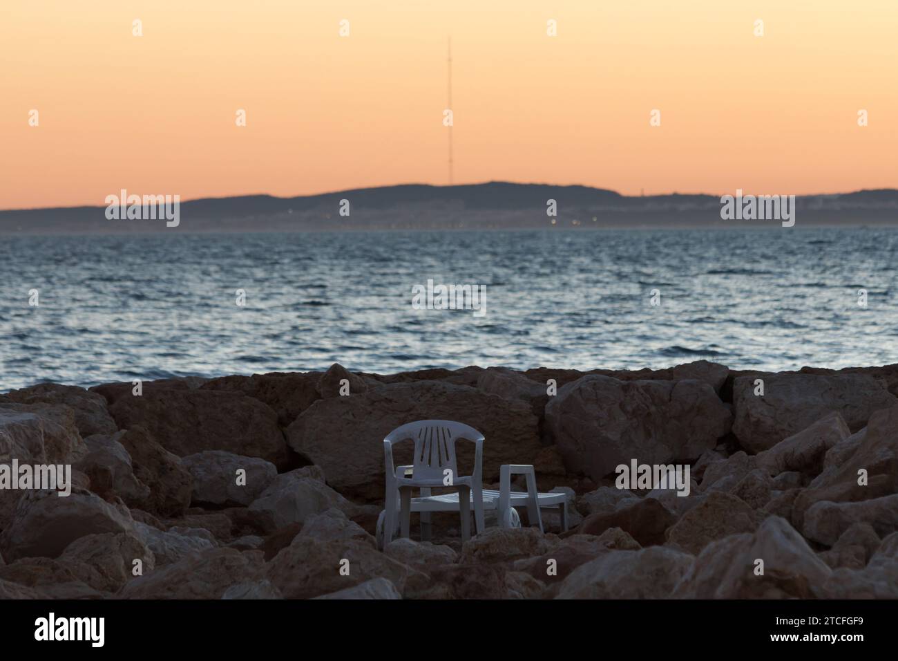 Sunset with a plastic lounger at the end of the breakwater in Santa Pola with Guardamar del Segura in the background and the highest antenna in Europe Stock Photo