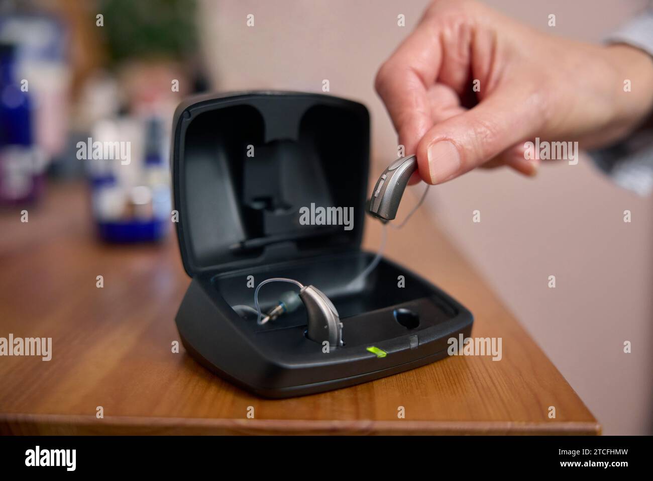 Close Up Of Person Picking Up Wireless Hearing Aid Or Device From Charging Case At Home Stock Photo