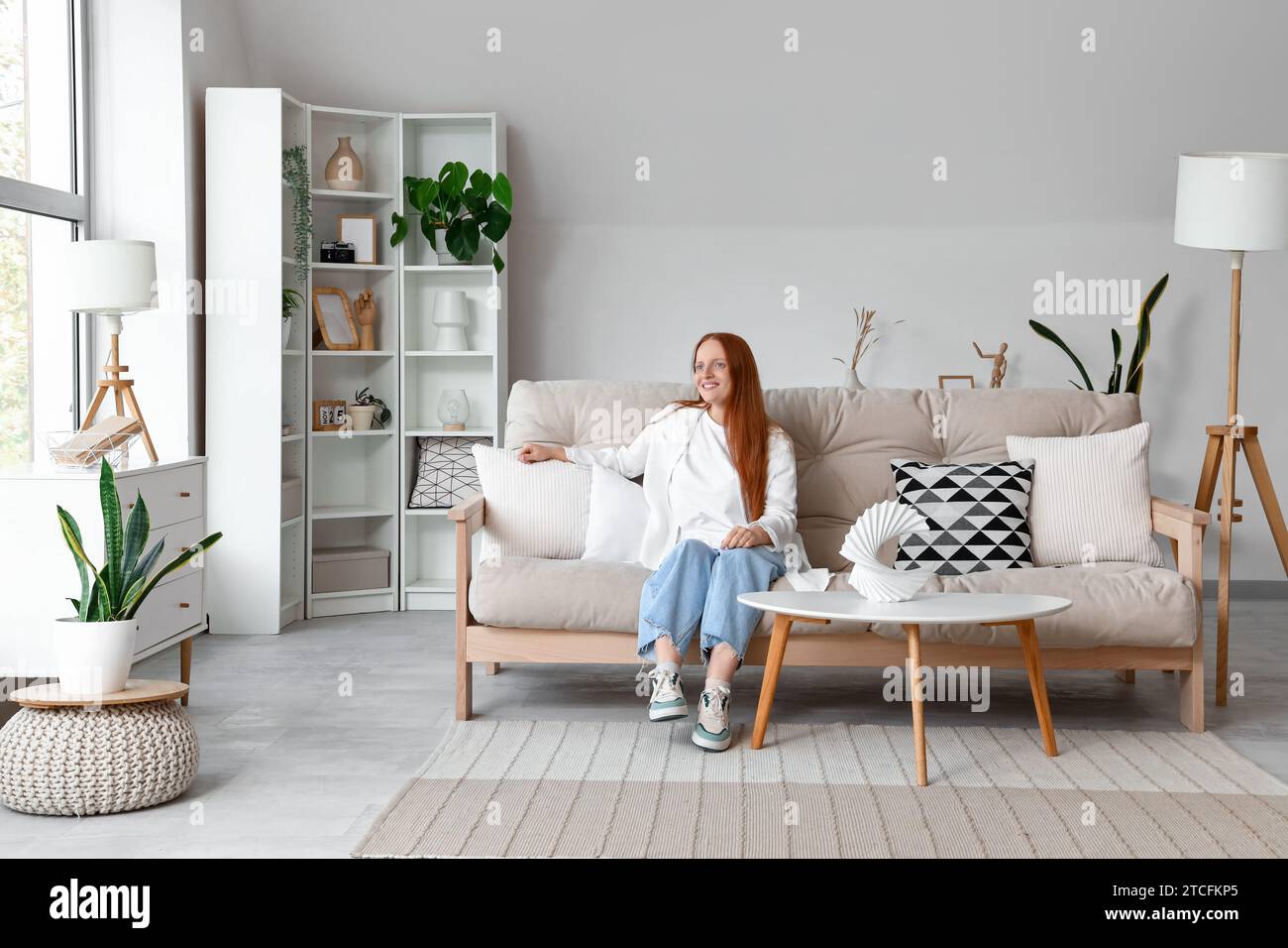 Pretty young woman sitting on white sofa in light living room Stock ...