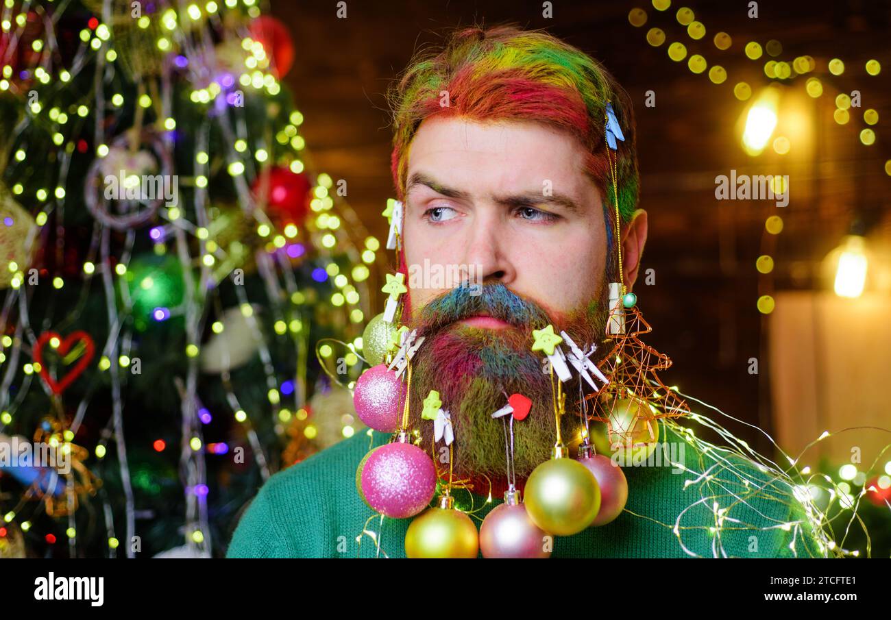 Merry Christmas and Happy New year. Serious man with decorated beard for New Year or Christmas. Bearded man with Christmas decoration balls in beard Stock Photo