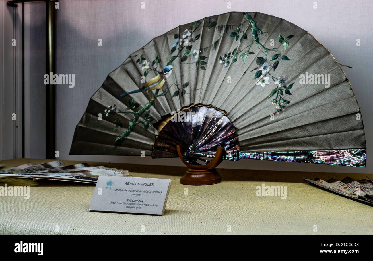 Ornate hand fan with mother-of-pearl and gold details on stand displayed in the Alcázar of Seville, The Royal Palace of Seville, Spain. Stock Photo